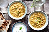 Two bowls of chana masala (chickpea curry) with unleavened bread and raita