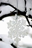 Snowflake decoration hanging from snow-covered tree