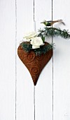 Two white roses and cedar twig with bird figurine on heart ornament on wall
