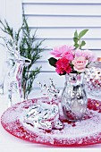 Vase in Bauernsilber-Optik mit Rosenstrauss und Rehfigur im Kunstschnee auf rotem Teller