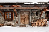 Winterstimmung - rustikales Natursteinhaus mit Holzlager vor Hauswand