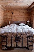 Simple bedroom in cabin - double bed with white bed linen and rustic wooden trunk with wrought iron fittings