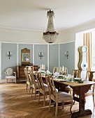 Chandelier above festively set dining table and upholstered, antique wooden chairs in country-style dining room with old herringbone parquet floor
