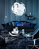 Wohnzimmer in Blau - Couchtisch mit geschwungenem Fussgestell und Sofa vor Wand in Streifenoptik unter kugelförmiger Hängeleuchte; im Vordergrund Drehsessel