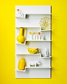 White wall-mounted shelving unit with ornaments on zigzag shelves on yellow wall