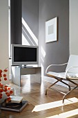 Flachbildschirm und Sessel mit Metallgestell in modernem Wohnzimmer mit hellgrau getönter Wand