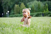 Kleines Mädchen im Gras sitzend, mit ratloser Gestik