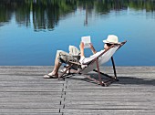 A young man sitting in a deck chair on a jetty reading a book