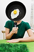 A woman holding a fried egg frying pan in front of her face