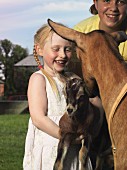 Zwei Mädchen mit Ziege und Zicklein auf dem Bauernhof