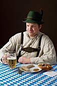 A stereotypical German man wearing lederhosen and eating white sausage with a beer