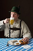 A stereotypical German man wearing lederhosen and eating white sausage with a beer