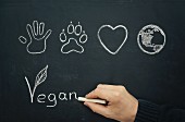 A hand writing the word 'Vegan' on a blackboard