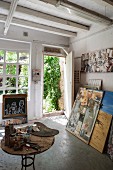 Artist's studio - painting utensils on table and pictures leaning against wall next to open door with view into garden