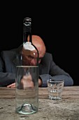 Deprimiert wirkender Geschäftsmann hinter einer Flasche Schnaps und halb volles Glas