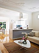 Retro coffee table on ethnic rug in front of sofa; partition kitchen counter to one side of open-plan interior with stucco ceiling