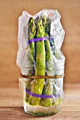 Keeping asparagus fresh: green asparagus spears in a plastic bag in a glass with a little water