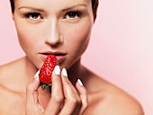 A woman holding a strawberry up to her mouth