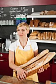A sales assistant holding a basket of baguettes in a bakery