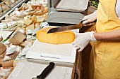 Verkäuferin schneidet Käse an der Käsetheke