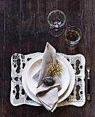 Name written on pebble on linen napkin and newspaper place mat with pattern of holes on rustic wooden table