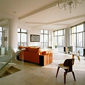 Designer-Stuhl aus Holz und Sofa mit orangefarbener Polsterung im Wohnzimmer einer Penthouse-Wohnung mit raumhohen Fenstern