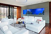 Modern sofa set with white leather covers and coffee table in lounge area; large aquarium incorporated in grey-tiled wall