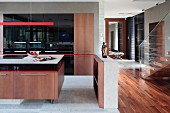 Detail of open-plan kitchen area, island counter with wooden base unit below red strip light in modern interior