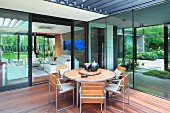 Terrace with round table and wooden slatted chairs on exotic wood deck in courtyard surrounded by contemporary house