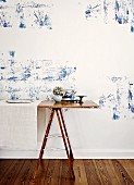 Improvisierter Tisch auf Metallböcken vor Wand, mit blauen Pflanzenstrukturen auf weißem Grund