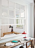 Rustikaler Schreibtisch mit Holzplatte und roter Tischleuchte im Retro Stil, vor Durchreiche mit offenem Sprossenfenster