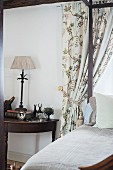 Four-poster bed next to antique, semicircular side table made from dark wood