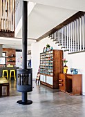 Free-standing wood-burning stove on concrete floor, sideboard and vintage shelving unit against staircase in open-plan interior