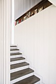 Staircase with concrete treads, white risers and narrow recess in wall decorated with framed photographs
