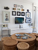 Blick über Rattan Coffeetable mit passenden Hockern in verschiedenen Grössen auf Flachbildschirm und Bildersammlung an Wand über weißem Sideboard