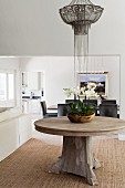 Bowl of orchids on round, solid-wood table below pendant lamp with metal beaded lampshade in open-plan elegant interior