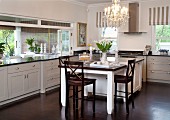 Dark wooden chairs at dining table adjoining counter in kitchen with white, country-house-style cabinets