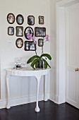 Orchid on white-painted console table below gallery of framed photos on wall
