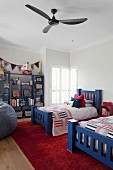 Twin beds with chunky, blue-painted wooden frames and patchwork bedspreads below ceiling fan