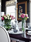 Table festively set with vases of flowers and silver candlesticks; painting on black wall in background