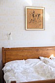 Bed with wooden headboard and white bed linen against wall with patterned wallpaper