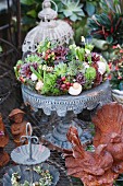 Decorative wreath of succulents with sempervivums on metal stand behind rust bird figurines