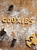 Cookie dough, cut-out letters and cutters on a floured wooden surface