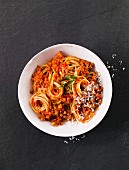 A bowl of spaghetti bolognese on a black surface (seen from above)