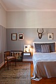 Rustic bedroom with hunting trophy above bed on wall painted pale grey