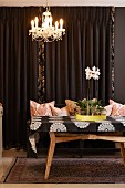 Orchids on yellow tray on retro wooden table below chandelier with beaded ornaments in front of brown curtain