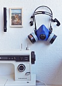 Ausschnitt einer Nähmaschine, darüber an Wand aufgehängte blaue Arbeitsmaske und Hundefoto