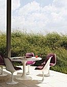 Tulip chairs and table on secluded, sunny terrace adjoining plant covered hill
