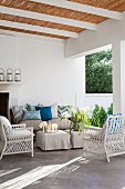 White wicker armchair and ottomans with loose covers in front of couch on roofed terrace with bamboo roof