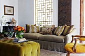 Ottoman with lime green cover and colourful bouquet in vase opposite sofa below window with wooden lattice framework; antique, upholstered armchair to one side